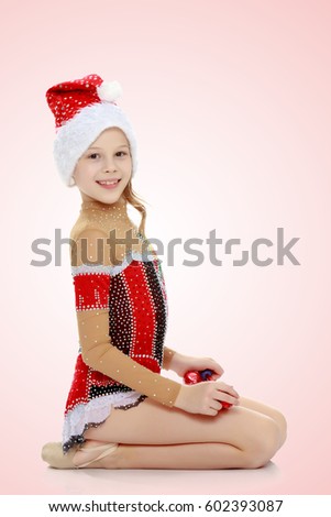 Cute little girl gymnast in a beautiful costume for competition, performs exercises with mace.Pale pink gradient background.