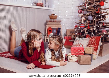 Girls sister friends hugging sitting at the Christmas tree, the concept of childhood, Christmas and New Year, on a light background