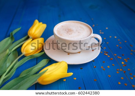 Coffee mug with yellow tulip flowers and notes good morning on blue rustic table from above, breakfast on Mother's day or Women's day .Spring  flowers bouquet