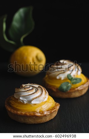 Lemon pie on the table with citrus fruits. Traditional french sweet pastry tart. Delicious, appetizing, homemade dessert with lemon cream. Copy space, closeup. Selective focus. Black background. Toned