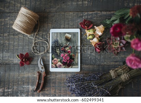 
Composition of flowers and a tablet lies on a wooden table, a top view. Tools for decoration and floristry