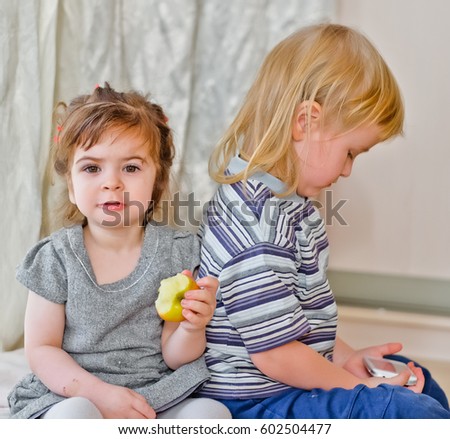 Little blonde long haired  boy with apple and brunette  girl with cellphone