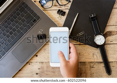 hands of man using phone white screen on top view on wooden table with office equipment