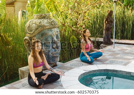 Young women practicing yoga during luxury yoga retreat in Asia, Bali, meditation, relaxation, getting fit, enlightening, green grass jungle background, buddha statue