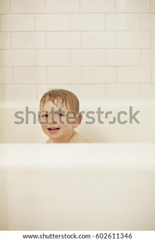 Young boy sitting in a bathtub, having a bath, smiling at camera