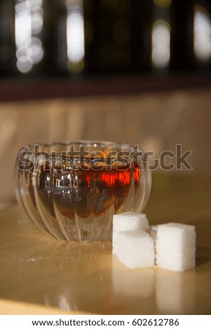 Black tea in a glass transparent bowl with pieces of white sugar in cubes. Small cup of tea on wooden table. Glass piala with double walls, double-bottomed bowl. Blurred background with bokeh.