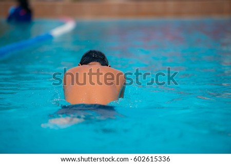 Teenager practices breast stroke swimming shot from his back side 