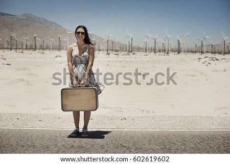 A young woman with a suitcase standing on the edge of the highway