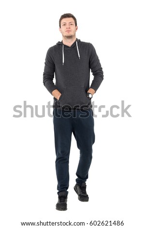 Front view of confident young man in sportswear walking with hands in pockets. Full body length portrait over white studio background. Royalty-Free Stock Photo #602621486
