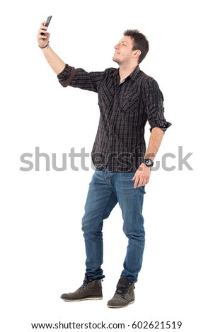 Casual man in jeans and plaid shirt taking photos with mobile phone.  Full body length portrait over white studio background.