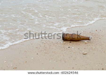 empty glass bottle lying on the sand beach with sea wave water. picture with copy space.