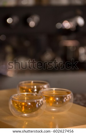 Green tea in a glass transparent bowl. Few small cups of tea on wood. Glass piala with double walls, double-bottomed bowl. Meal, aperitif, repast. Blurred background with bokeh.