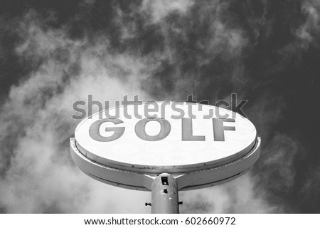 Old style vintage golf sign on pole with bold big lettering and golf balls on sign. Black and white.   Sky and clouds background. 
