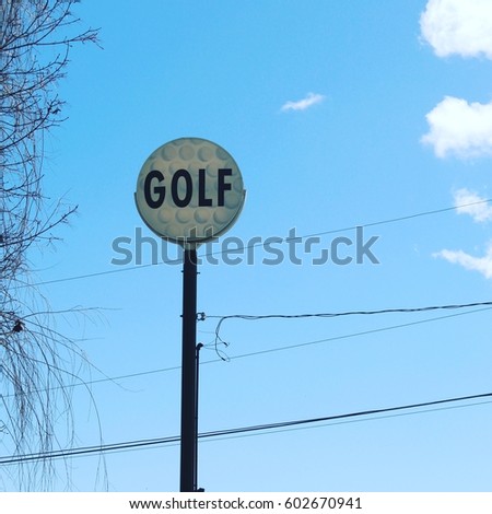 Old style vintage golf sign on pole with bold big lettering and golf balls design on sign.   Blue sky white clouds background.