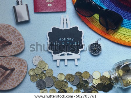 Travel and holiday concept. Top view of passport, coins spill, compass, sunglasses, hat and flip flop with board written HOLIDAY TIPS & TRICKS. Vintage editing.