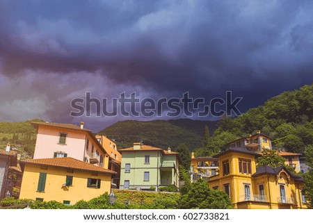 Beautiful toned cityscape of italian city with building, green mountain, trees and dramatic cloudy sky before the rain