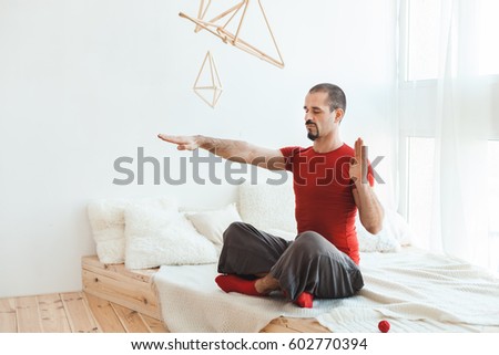 Man in a yoga pose in nirvana, he sits on the bed in the bedroom.