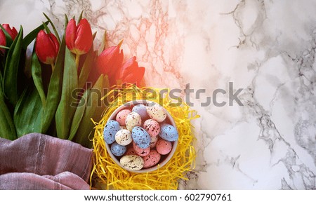 Easter eggs and spring tulip flowers on white marble, artistic glow effect. Spring / Summer and Easter day concept.
