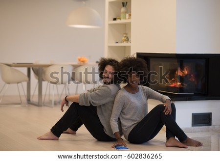 beautiful young multiethnic couple with tablet computer sitting on the floor of their luxury home in front of fireplace at autumn day