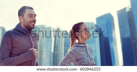 fitness, sport, people, technology and lifestyle concept - happy couple running and listening to music in earphones over singapore city skyscrapers background