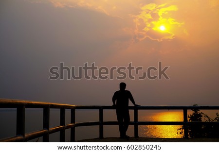 Silhouette of man on vibrant sunset. He touch the iron rail with the sunset.