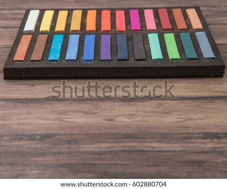 Chalk pastel stick in black container box over wooden background