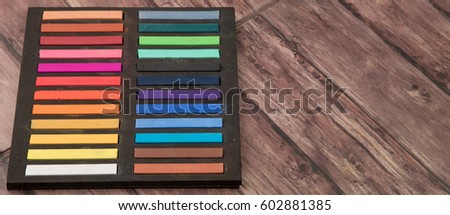 Chalk pastel stick in black container box over wooden background