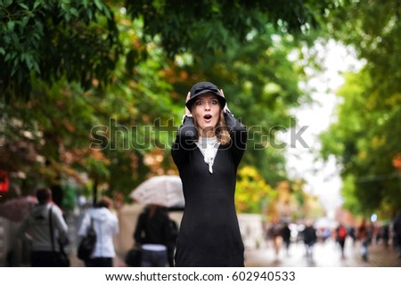 Portrait of a beautiful girl in a black dress and wearing a hat in rainy weather against the backdrop of the bright greenery of a city street. Saratov, Russia.