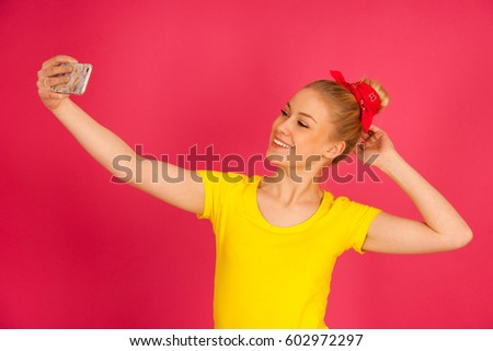 Beautiful young blond teenage woman in yellow t shirt  taking selfie over pink background.