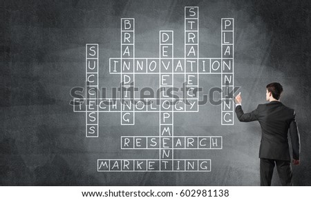 Businessman standing with back and drawing crossword on blackboard