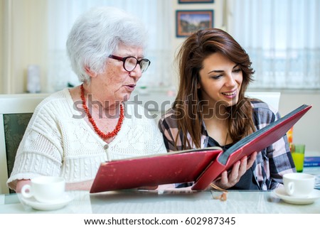 Grandma and her granddaughter looking at photo album together at home.