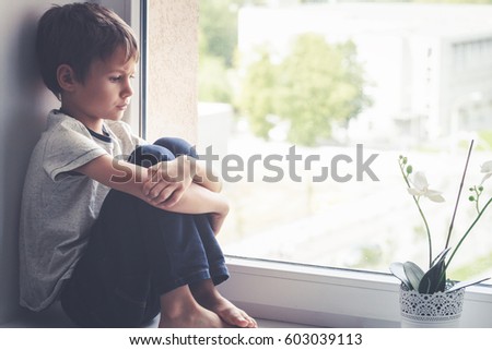Sad little kid sitting on window shield Royalty-Free Stock Photo #603039113