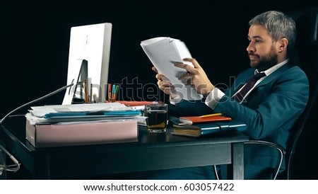 Frustrated bearded businessman looks through business papers. Black background