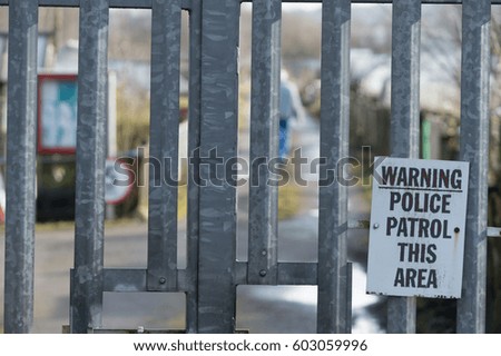 Police Patrol This Area sign on metal gates with blurred allotments in the background