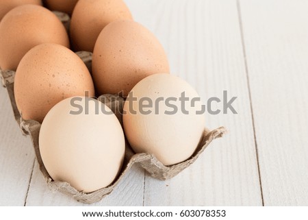 Fresh eggs in carton package on white wood background. Horizontal photo