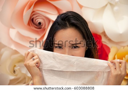 Shy young woman hiding behind the handkerchief on paper roses background.