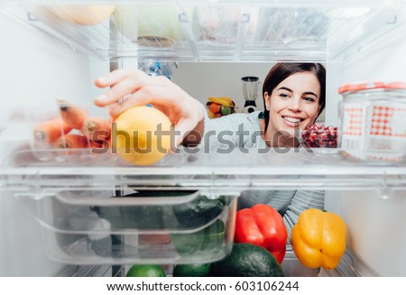 Smiling woman taking a fresh lemon out of the fridge, healthy food concept Royalty-Free Stock Photo #603106244