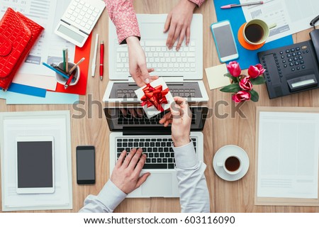 Woman receiving a beautiful gift from her male colleague while working in the office; relationships concept, top view