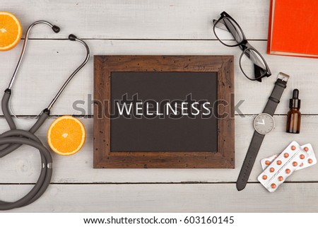 Medecine concept - Blackboard with text "Wellness", pills, book and stethoscope on white wooden background Royalty-Free Stock Photo #603160145