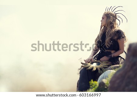 Fantastic woman holding a sun in his hands. Magic and fairy sitting in the mountains on a background of smoke. Fantasy story.