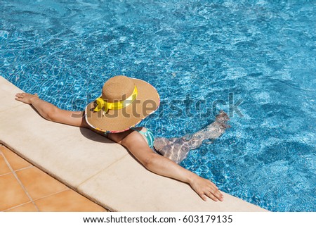 Woman in hat relaxing on the edge of swimming pool