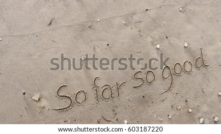 Handwriting words "So far So good." on sand of beach