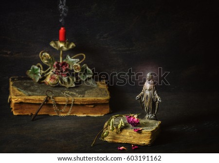 Classic still life with Virgin Mary statue placed with old bible,dry rose,candle holder and vintage key on dark background.Spiritual atmosphere concept.