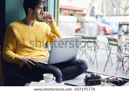Handsome well dressed male owner of photography agency communicating with client talking about photo session arranging meeting through phone call while sitting in coffee shop with laptop computer