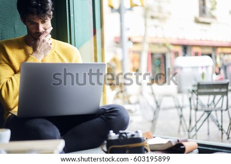 Thoughtful male freelancer working on project for online issue creating text and descriptions for retro photo session sitting in cafe indoor using laptop computer and wireless connection to network