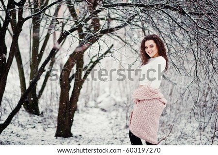Curly brunette girl background falling snow, wear on warm knitted sweater, black mini skirt and wool stockings. Model on winter. Fashion portrait at snowy weather.  toned photo.