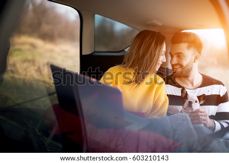 Nice cheerful couple relaxing in car trunk after long trip. Sunset light on background.