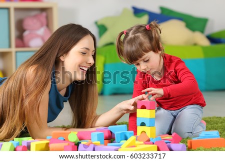 Mother and daughter playing together with colorful construction toys on a carpet on the floor af a bedroom at home Royalty-Free Stock Photo #603233717