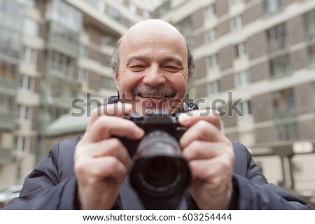 An elderly man with a mirrorless camera chooses a frame on the street