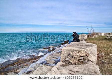 Woman photographer bundled in winter clothes and snaping pictures of the waves as they splash up from Chicago's Lake Michigan south shore on a chilly winter day